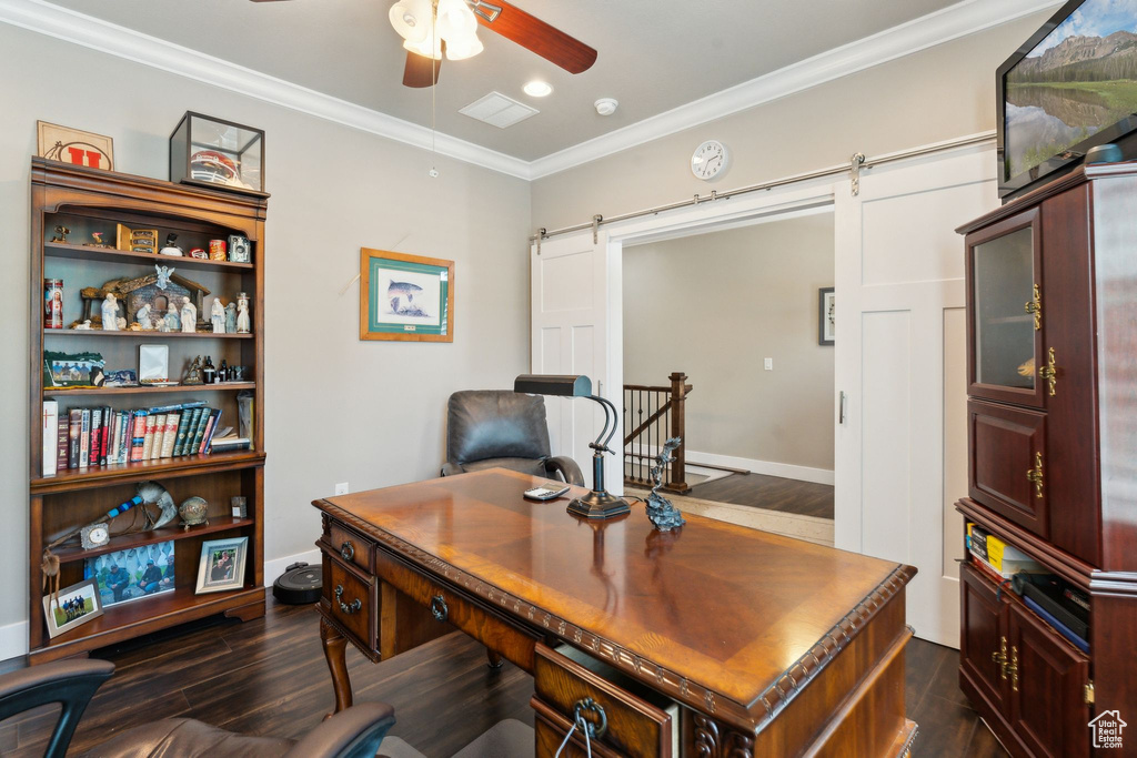 Office area with a barn door, a ceiling fan, dark wood-style flooring, crown molding, and baseboards