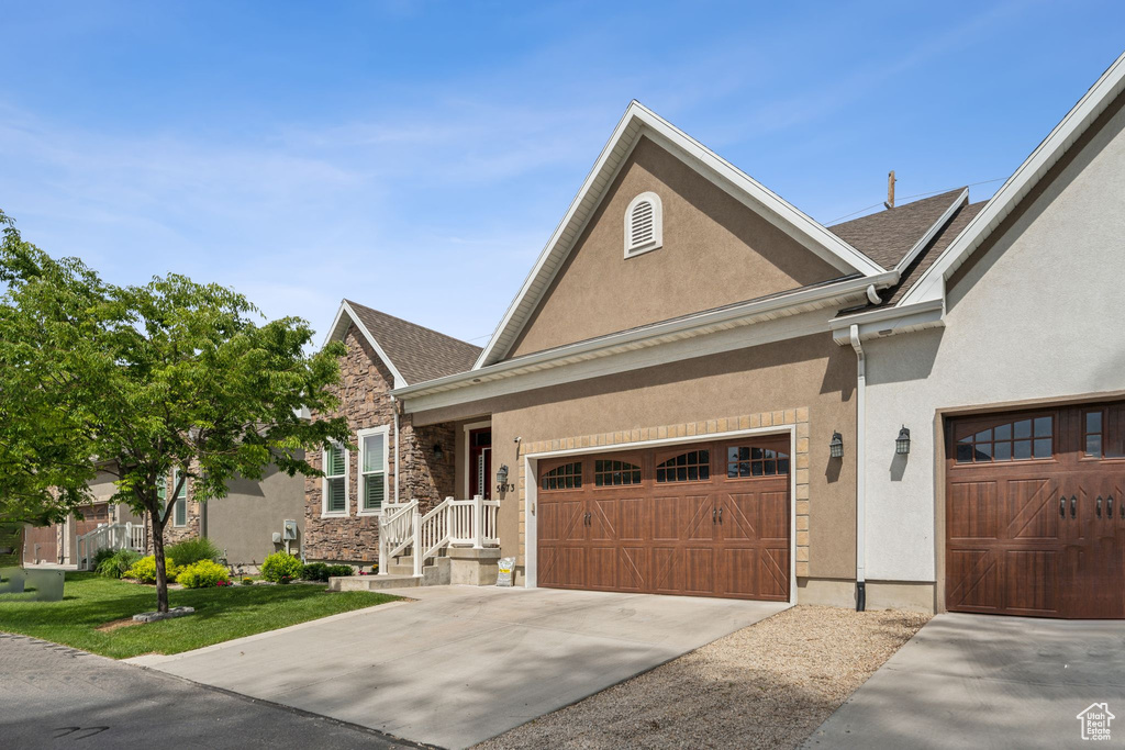 View of front of home with stucco siding, concrete driveway, a front lawn, a garage, and stone siding