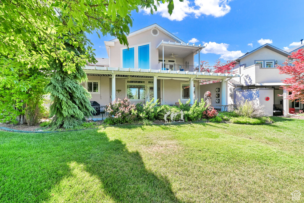 View of front of home with stucco siding, a front lawn, a patio, a ceiling fan, and a balcony