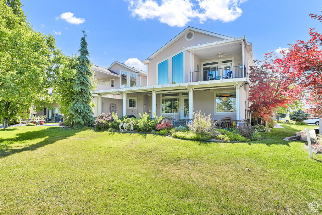 View of front of property featuring a balcony, a ceiling fan, a front yard, and stucco siding