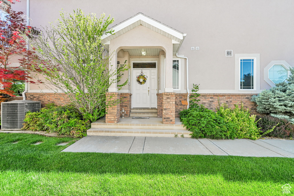 View of exterior entry featuring stucco siding, a yard, and brick siding