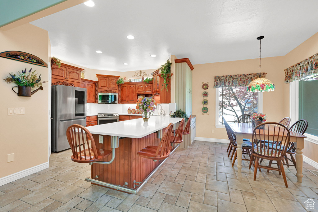 Kitchen featuring stainless steel appliances, stone tile flooring, a peninsula, brown cabinets, and light countertops