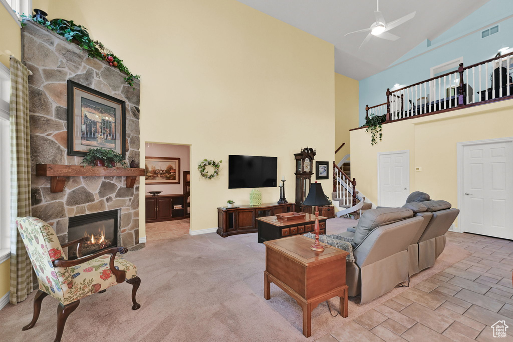 Living room featuring a stone fireplace, high vaulted ceiling, stairway, and ceiling fan
