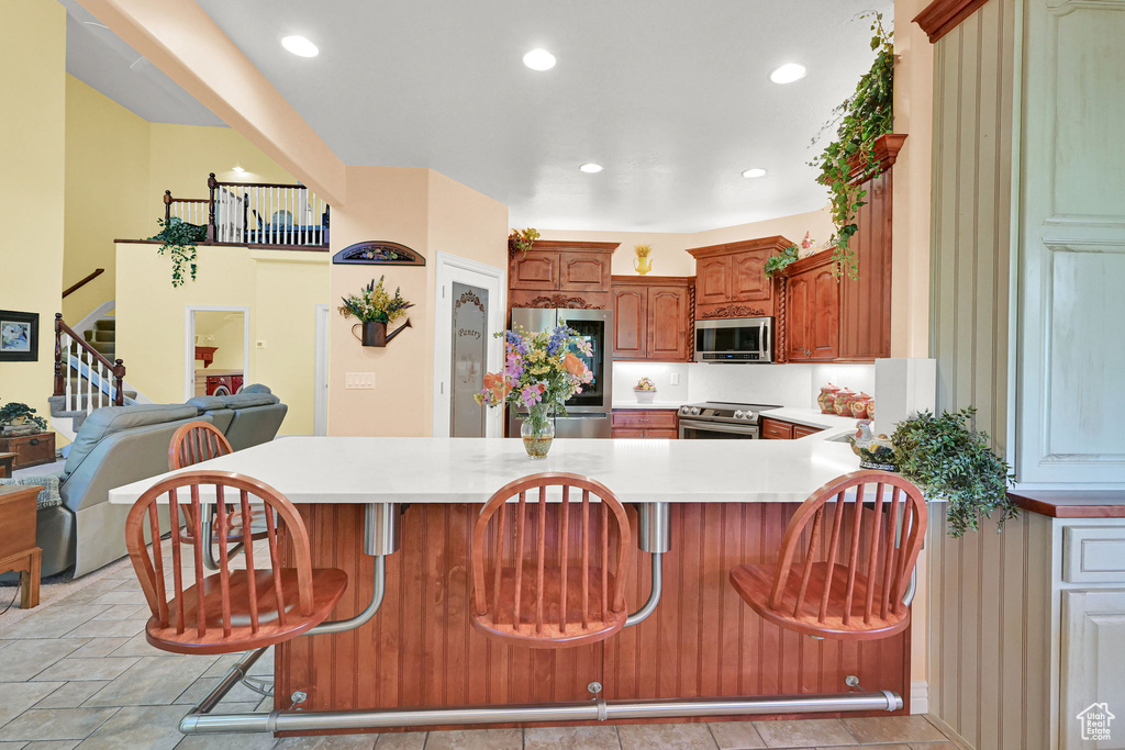 Kitchen with appliances with stainless steel finishes, light countertops, a breakfast bar area, a peninsula, and recessed lighting