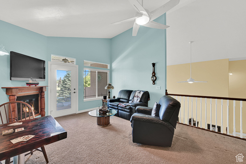 Living area featuring a ceiling fan, vaulted ceiling, carpet flooring, and a glass covered fireplace