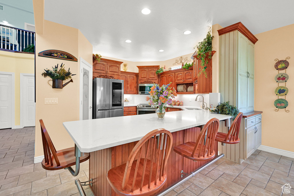 Kitchen featuring appliances with stainless steel finishes, a peninsula, light countertops, a breakfast bar area, and recessed lighting
