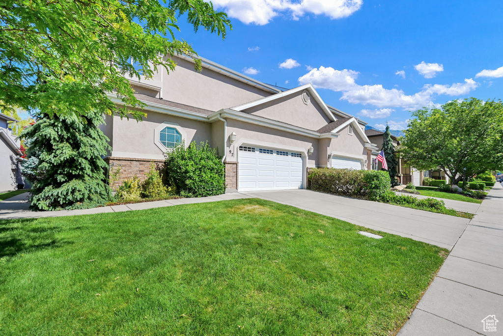 Ranch-style house with stucco siding, driveway, a front lawn, an attached garage, and brick siding