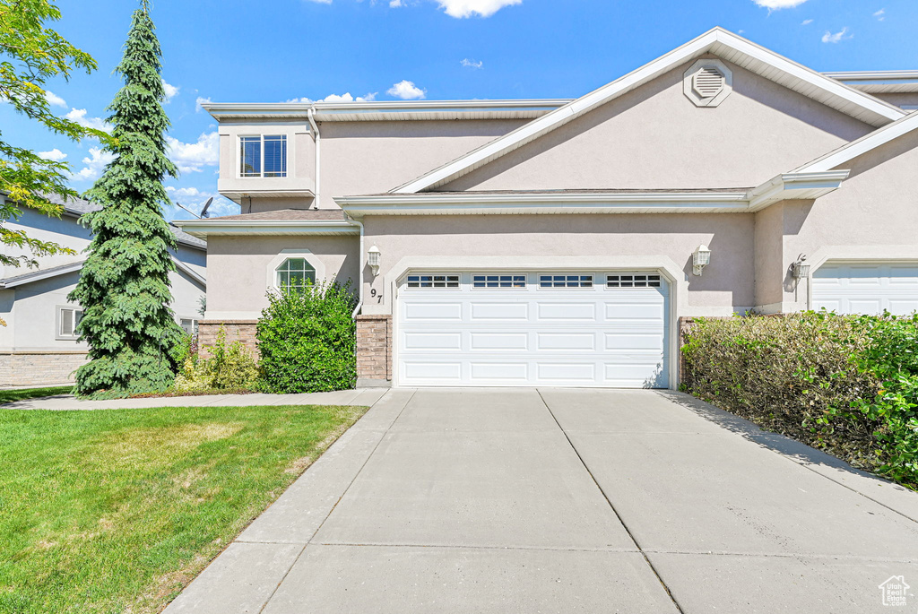 Traditional-style home with stucco siding, concrete driveway, an attached garage, and a front lawn