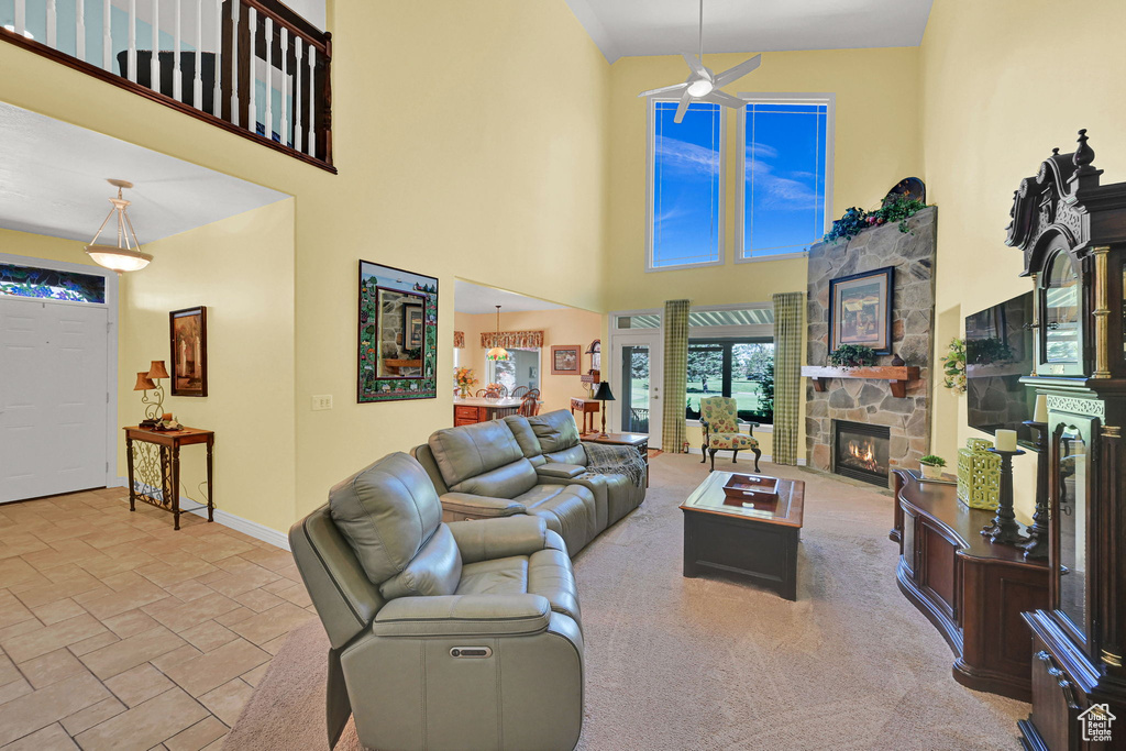 Living area with a towering ceiling, a fireplace, ceiling fan, and stone tile flooring