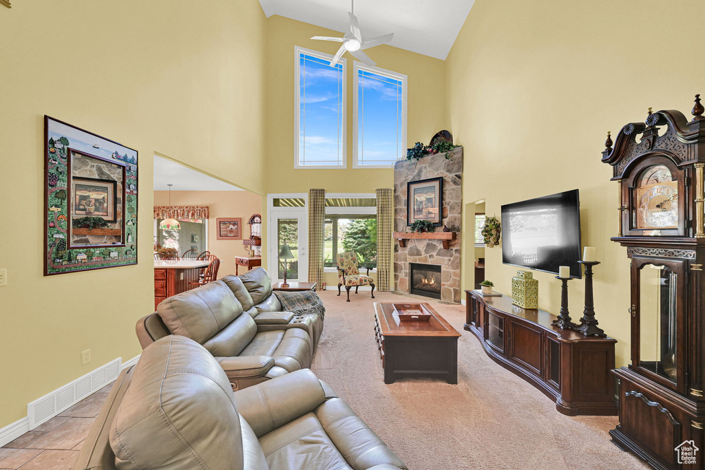 Living area with a high ceiling, a ceiling fan, and a stone fireplace