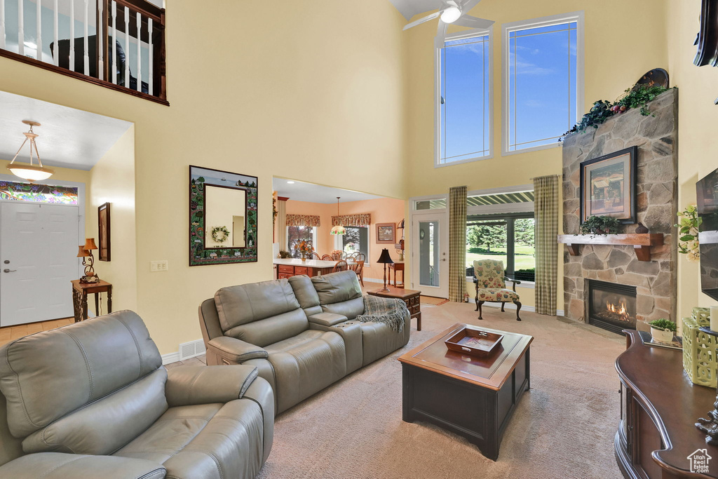 Carpeted living area featuring a fireplace, a high ceiling, and a ceiling fan