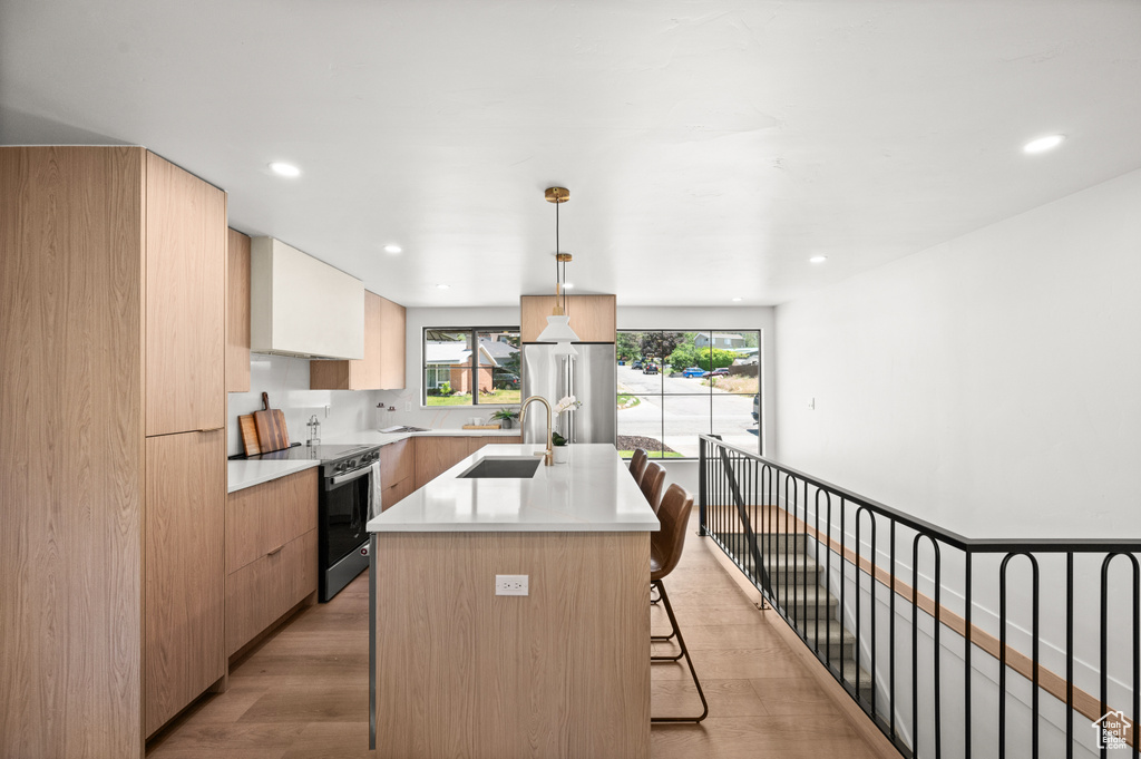 Kitchen with stainless steel range with electric stovetop, a breakfast bar, a kitchen island with sink, modern cabinets, and light countertops
