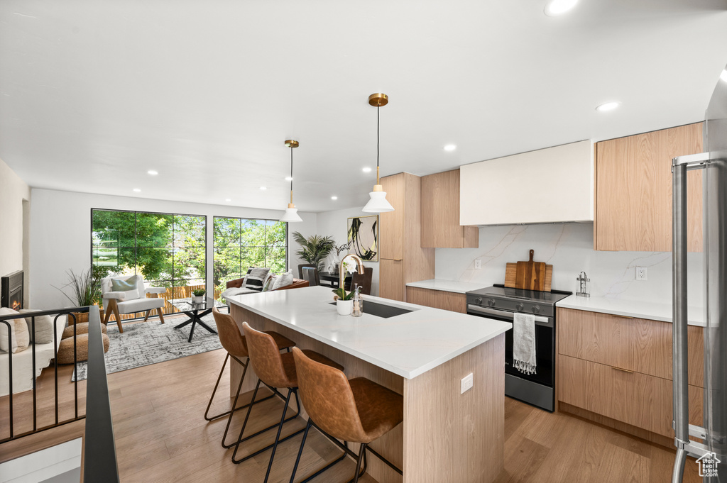 Kitchen featuring stainless steel range with electric stovetop, modern cabinets, recessed lighting, a kitchen island with sink, and light wood-style floors