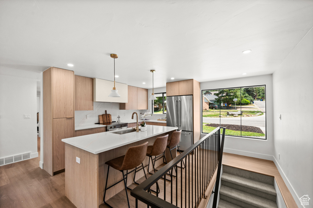 Kitchen featuring stainless steel appliances, light wood-style flooring, a kitchen breakfast bar, modern cabinets, and a center island with sink