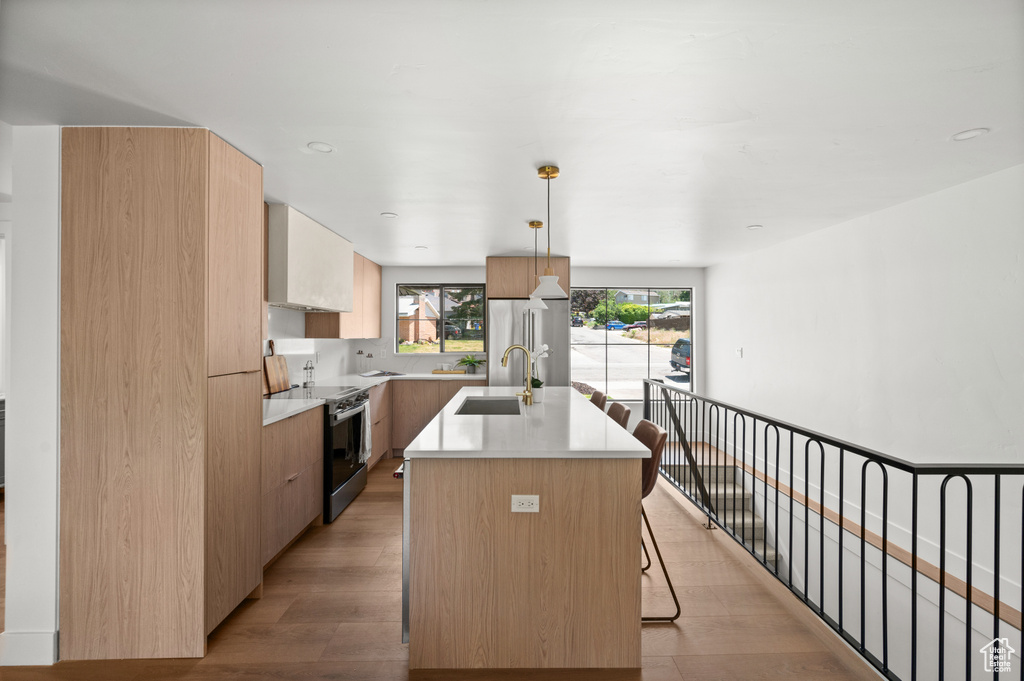Kitchen featuring stainless steel appliances, an island with sink, modern cabinets, light countertops, and a kitchen bar