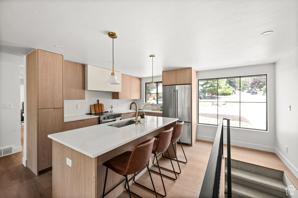 Kitchen with stainless steel appliances, a kitchen breakfast bar, light wood finished floors, and an island with sink