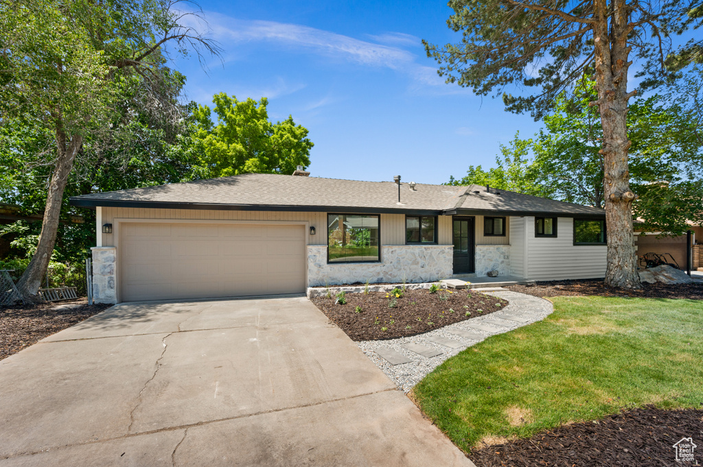Ranch-style home featuring stone siding, an attached garage, concrete driveway, a front yard, and roof with shingles