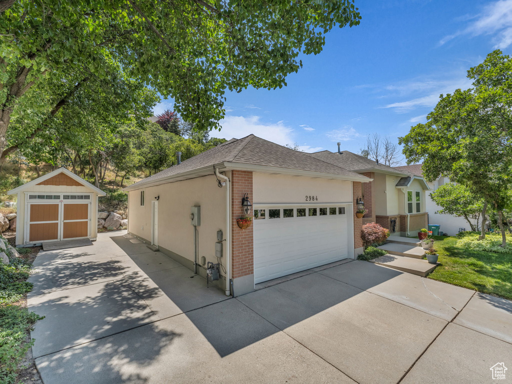 View of front of property featuring roof with shingles, a storage unit, brick siding, concrete driveway, and stucco siding