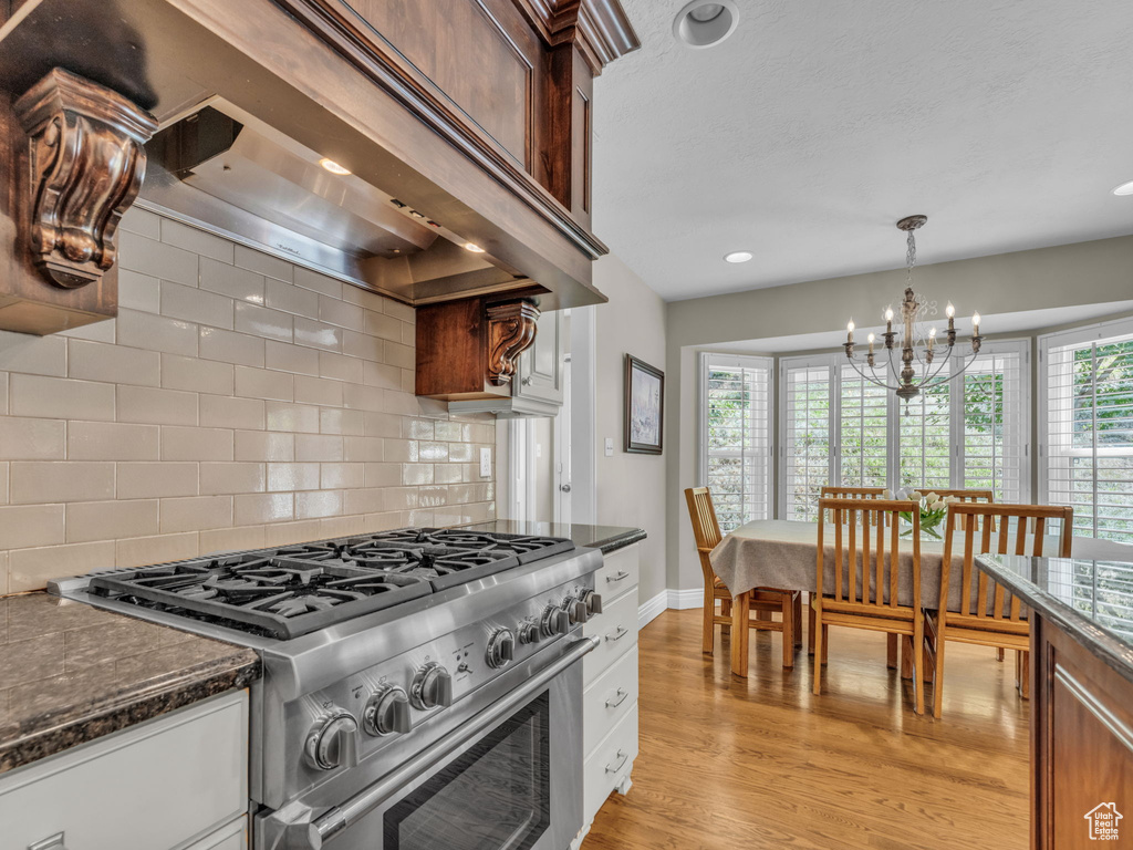 Kitchen featuring high end stainless steel range, custom range hood, decorative backsplash, light wood-style floors, and a chandelier