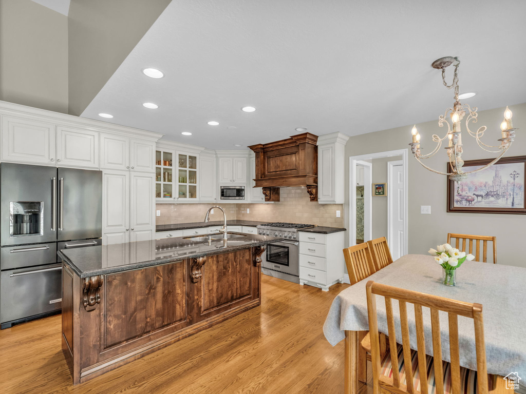 Kitchen featuring high quality appliances, light wood-type flooring, backsplash, white cabinetry, and recessed lighting