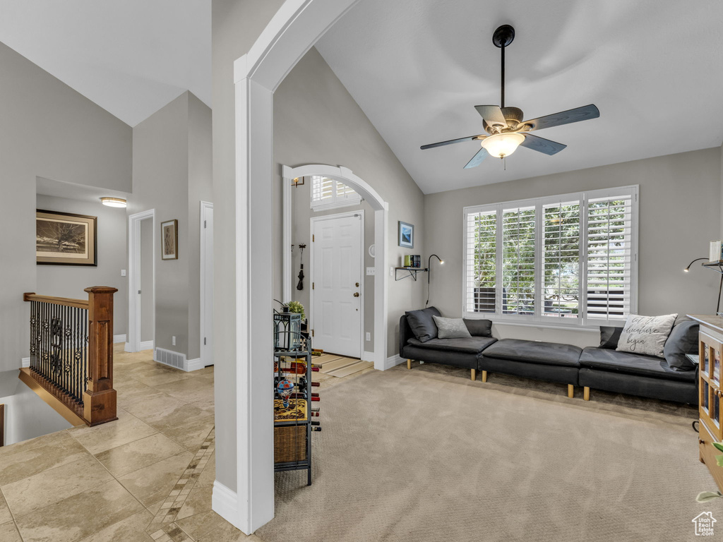 Living room featuring arched walkways, high vaulted ceiling, a ceiling fan, and light carpet