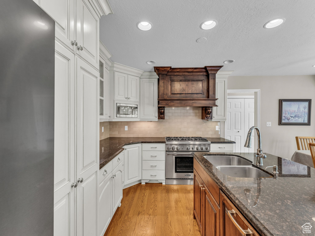 Kitchen featuring appliances with stainless steel finishes, light wood-type flooring, tasteful backsplash, dark stone countertops, and white cabinets