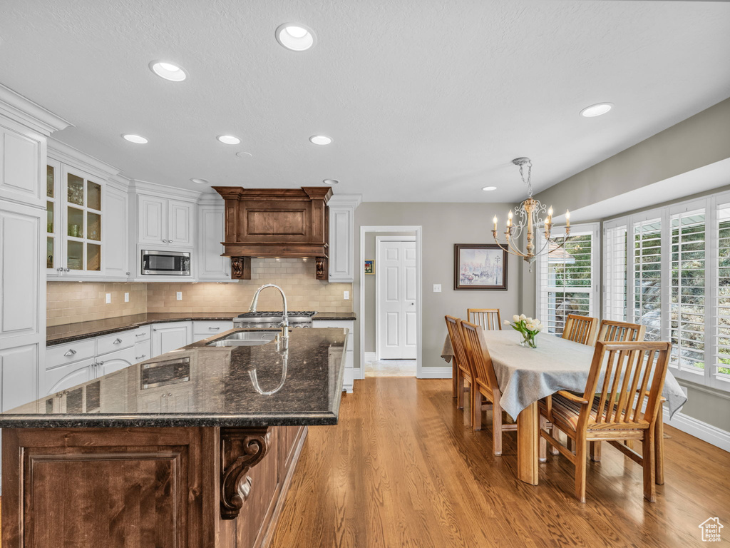 Kitchen with stainless steel microwave, a chandelier, light wood finished floors, recessed lighting, and decorative backsplash