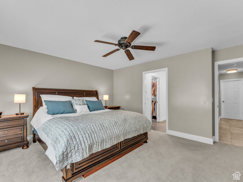 Bedroom with light carpet, a spacious closet, a ceiling fan, and a closet
