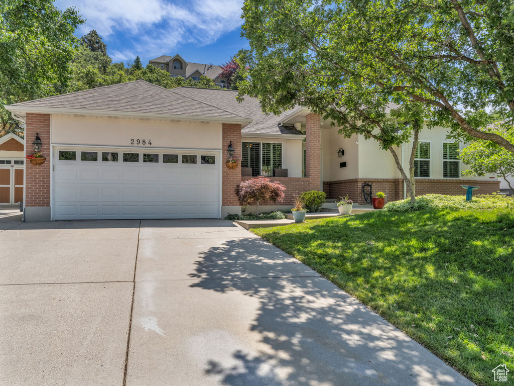 View of front facade featuring brick siding, concrete driveway, a front lawn, and a garage