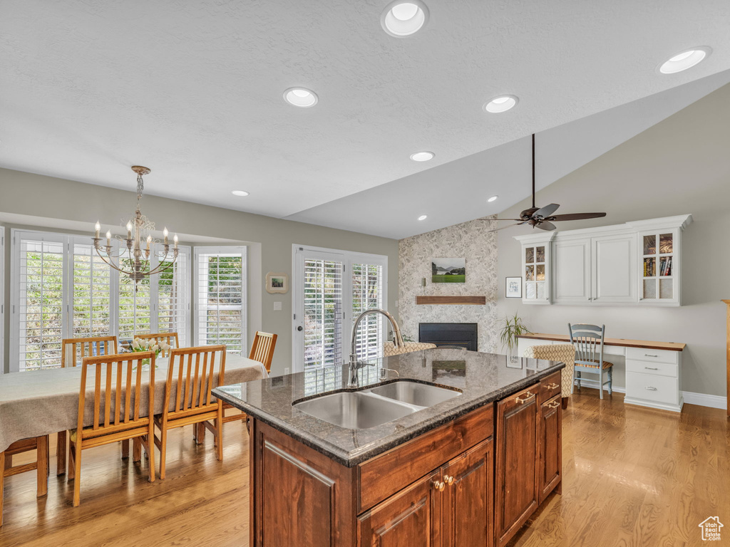 Kitchen with a large fireplace, a ceiling fan, lofted ceiling, light wood finished floors, and dark stone counters