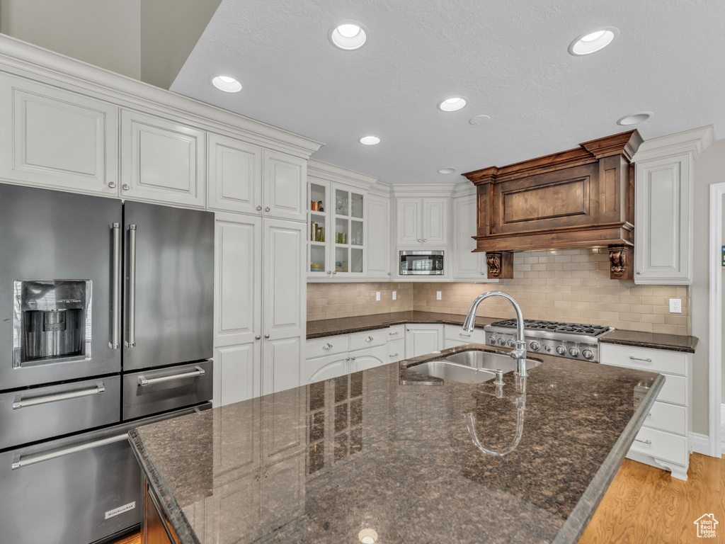 Kitchen featuring appliances with stainless steel finishes, a center island with sink, light wood finished floors, white cabinetry, and tasteful backsplash