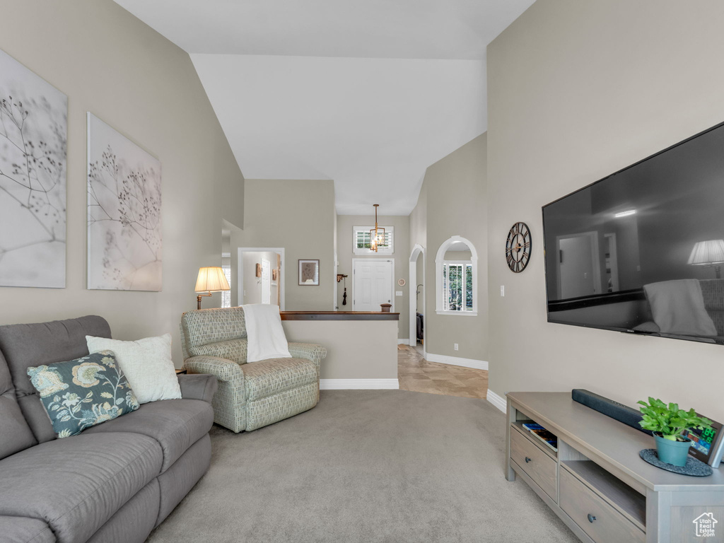 Living room featuring light colored carpet, high vaulted ceiling, a chandelier, and arched walkways