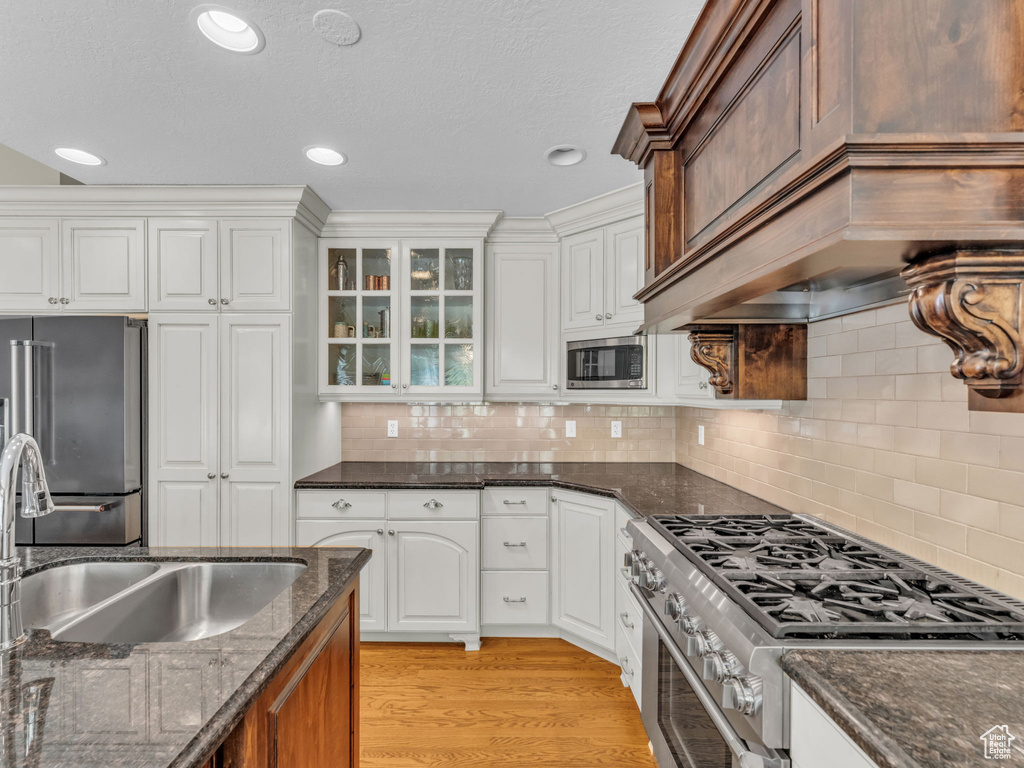 Kitchen with appliances with stainless steel finishes, white cabinetry, glass insert cabinets, dark stone counters, and recessed lighting