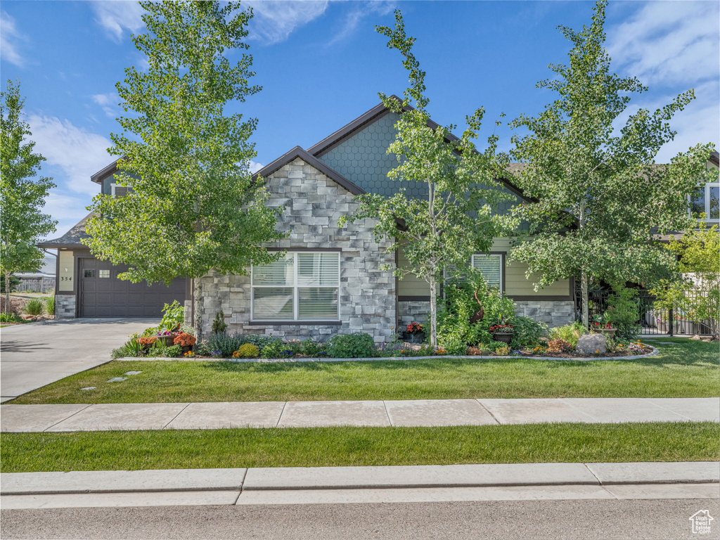 View of front of property featuring stone siding, driveway, and a front yard