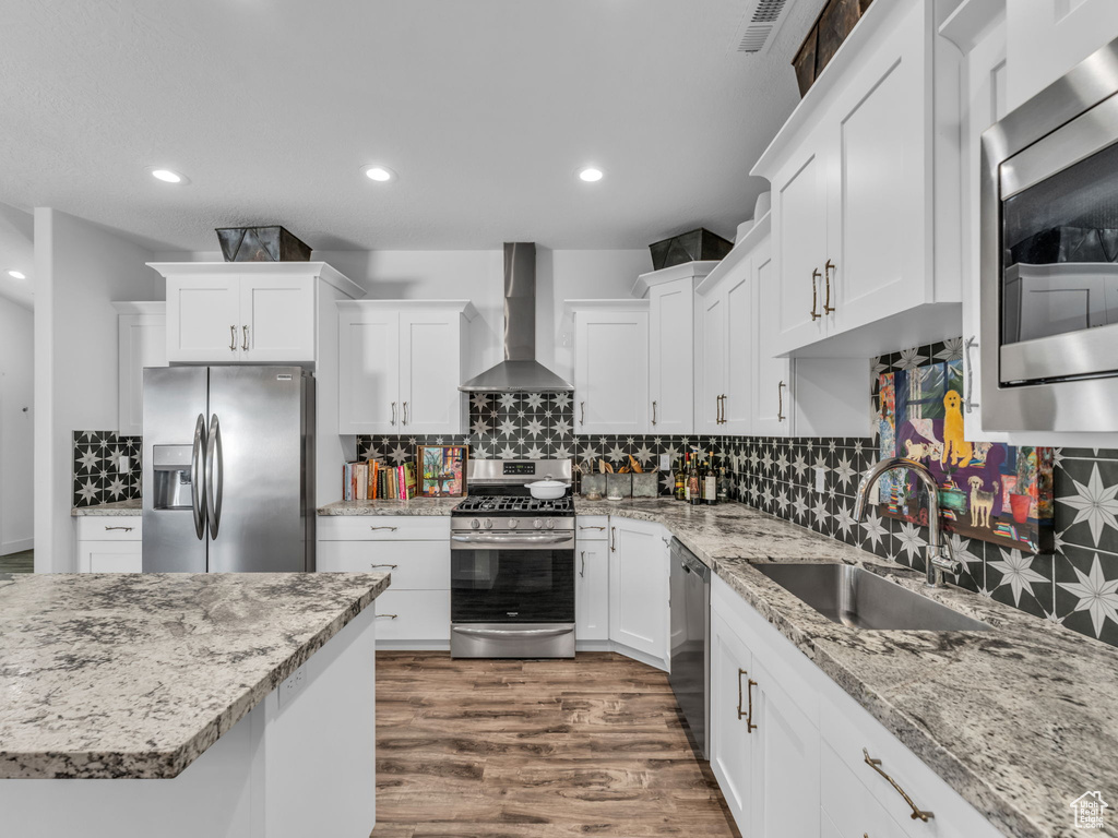 Kitchen with stainless steel appliances, wall chimney exhaust hood, dark wood-style flooring, decorative backsplash, and recessed lighting