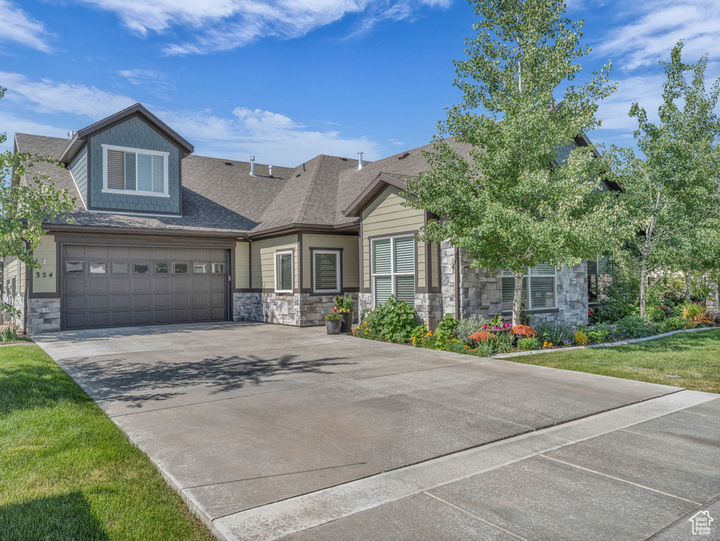 View of front of house featuring stone siding, concrete driveway, a garage, and a shingled roof
