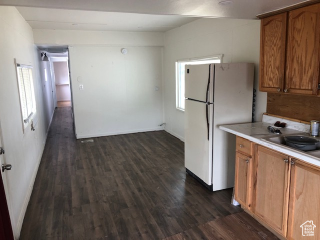 Kitchen with freestanding refrigerator, dark wood finished floors, light countertops, brown cabinets, and healthy amount of natural light