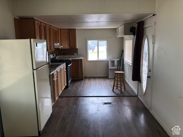 Kitchen featuring freestanding refrigerator, stainless steel range with gas stovetop, brown cabinets, and dark wood-type flooring