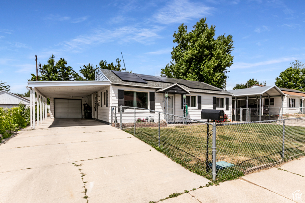 View of front of property featuring concrete driveway, roof mounted solar panels, a carport, and an attached garage