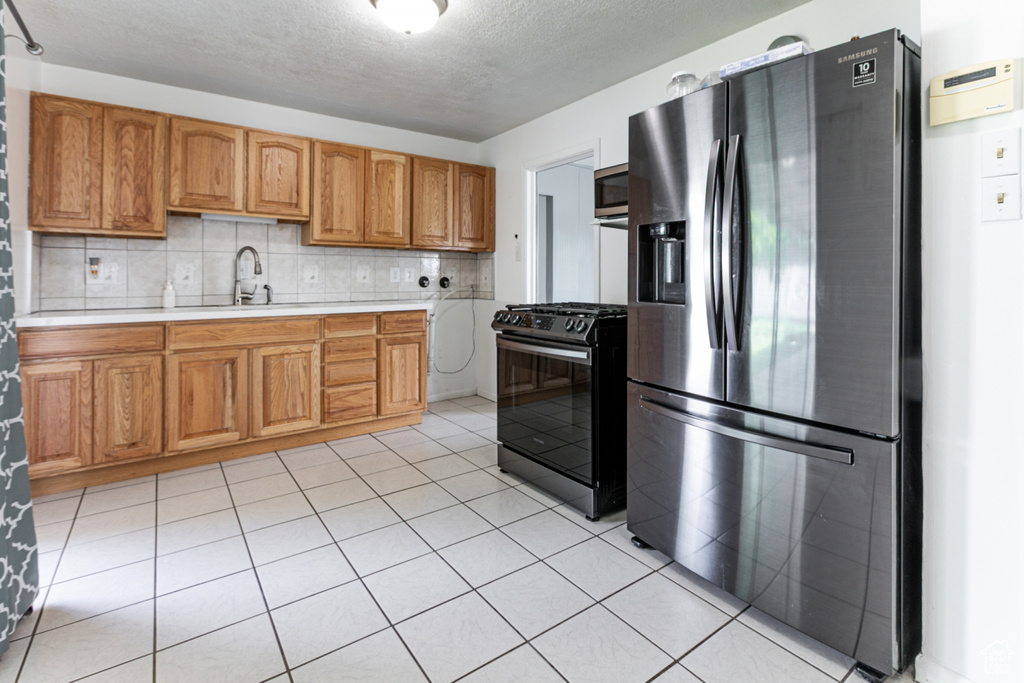 Kitchen with appliances with stainless steel finishes, light countertops, a textured ceiling, brown cabinetry, and tasteful backsplash