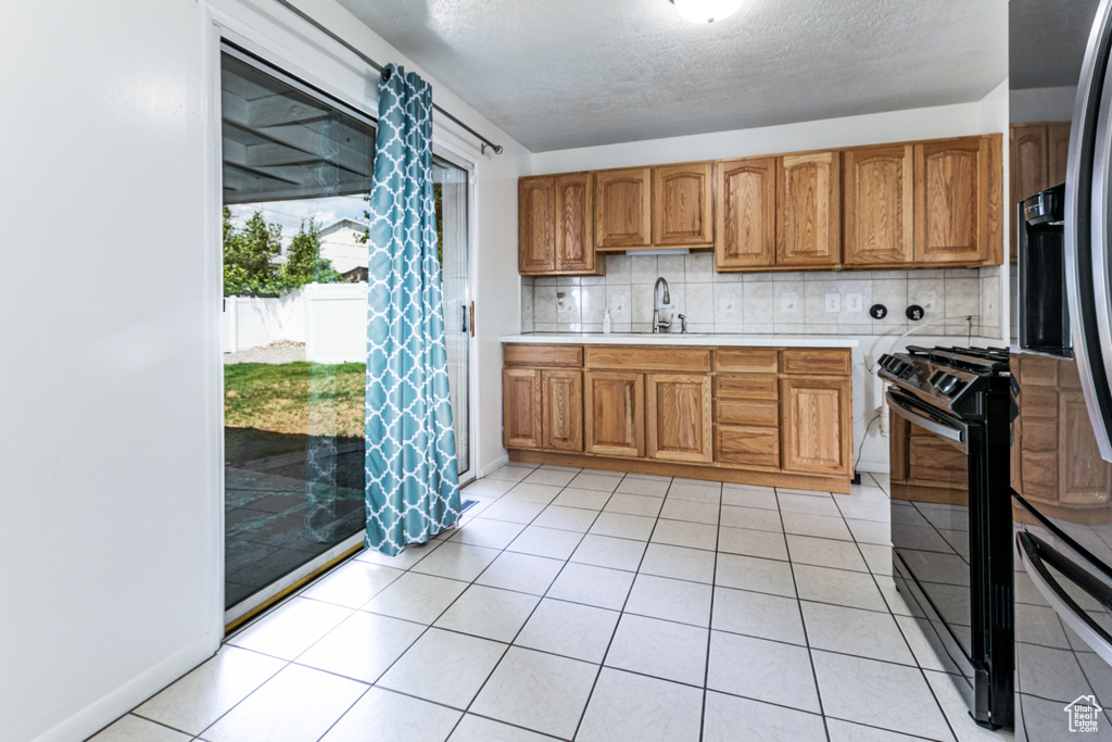 Kitchen featuring black range with gas cooktop, refrigerator with ice dispenser, light countertops, brown cabinetry, and a textured ceiling