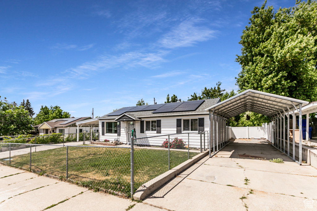 View of front of house featuring a fenced front yard, a carport, concrete driveway, and solar panels