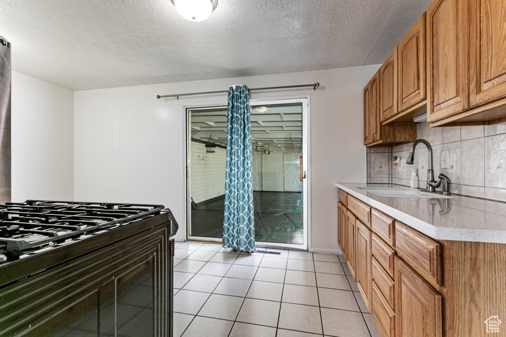 Kitchen with backsplash, black range with gas stovetop, a textured ceiling, light tile patterned floors, and brown cabinetry