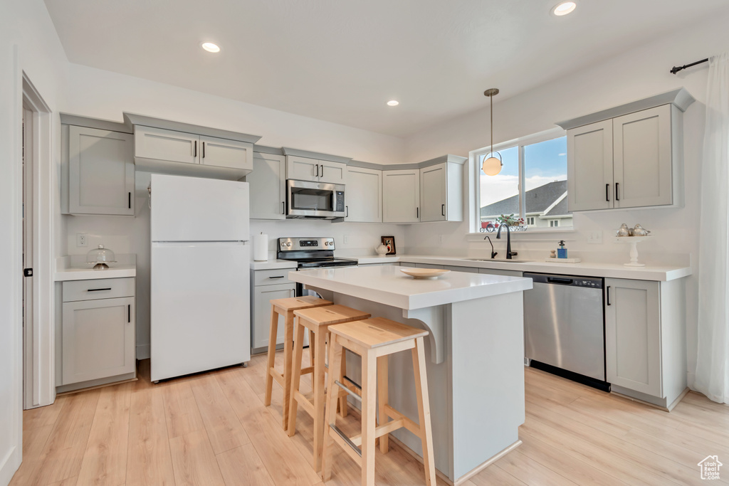 Kitchen with stainless steel appliances, gray cabinetry, a breakfast bar, light countertops, and light wood-style floors