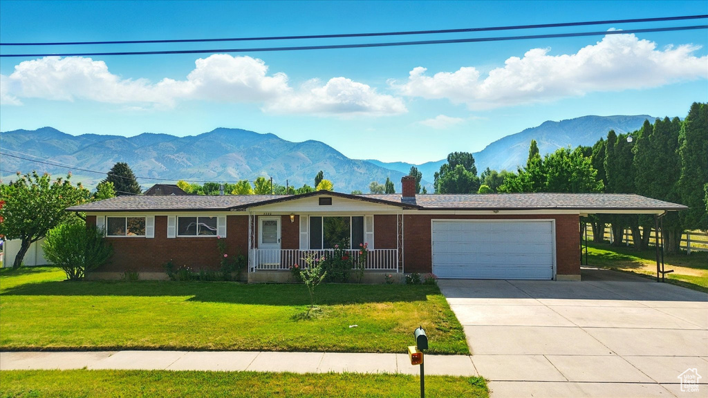 Single story home with an attached garage, a mountain view, concrete driveway, a chimney, and brick siding