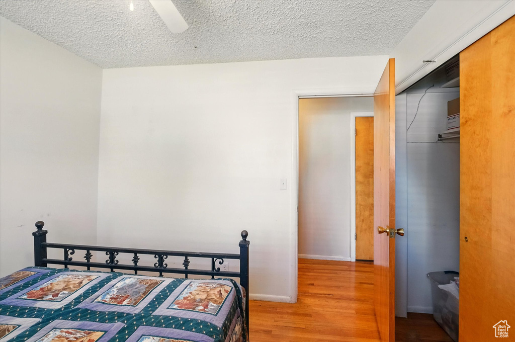 Bedroom with wood finished floors, a textured ceiling, a closet, and a ceiling fan