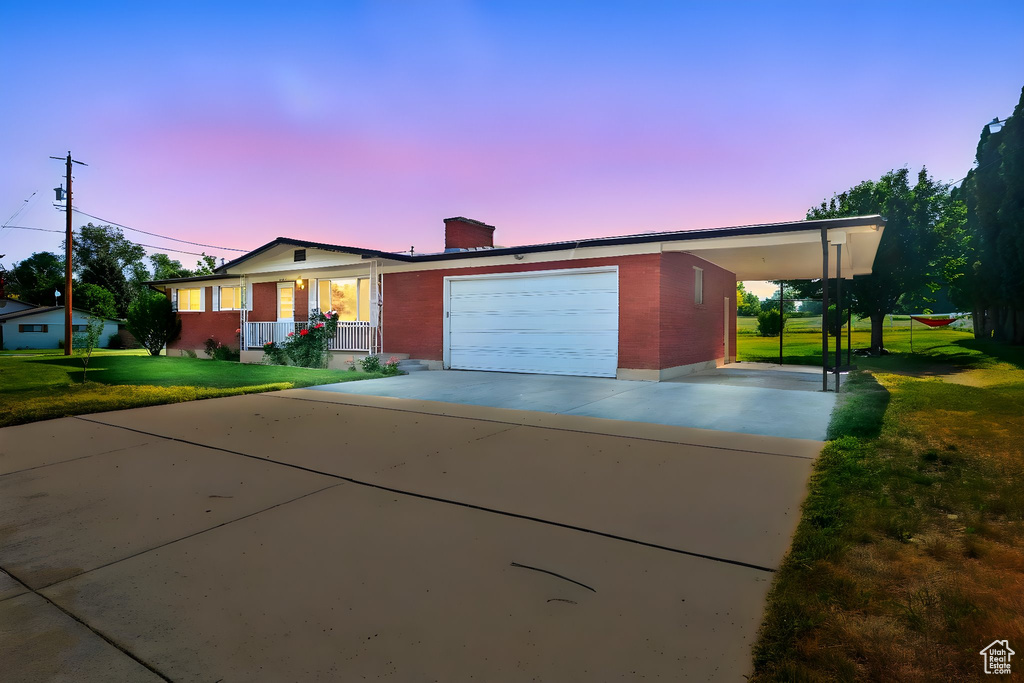 Single story home featuring a porch, a carport, concrete driveway, a yard, and an attached garage