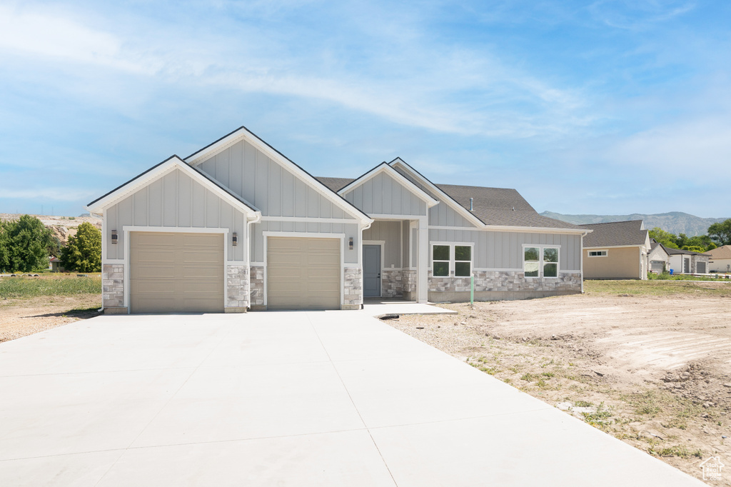 Craftsman-style house featuring an attached garage, stone siding, driveway, and a mountain view