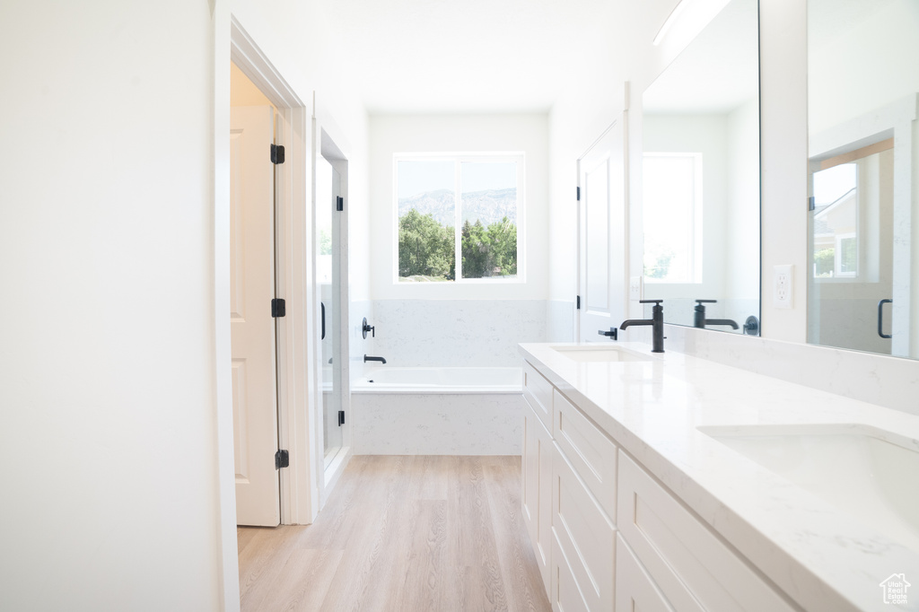 Bathroom featuring a garden tub, wood finished floors, double vanity, and a stall shower