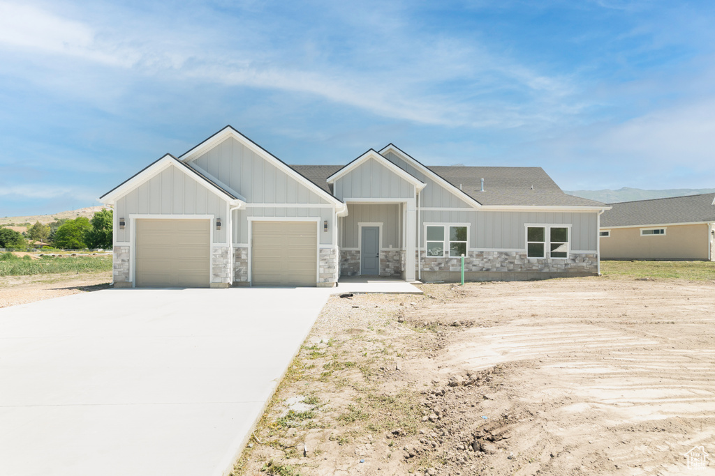 View of front facade featuring an attached garage, stone siding, concrete driveway, board and batten siding, and a shingled roof